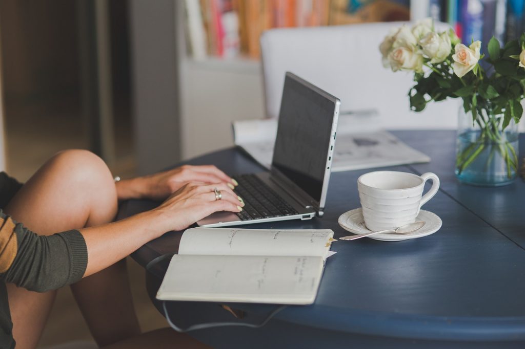 A woman sat at a table writing on a laptop.