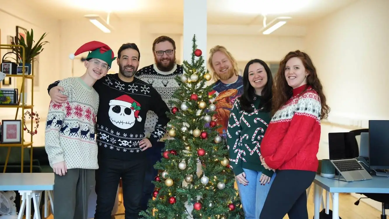 A team photo of the wonder agency in christmas jumpers next to a christmas tree