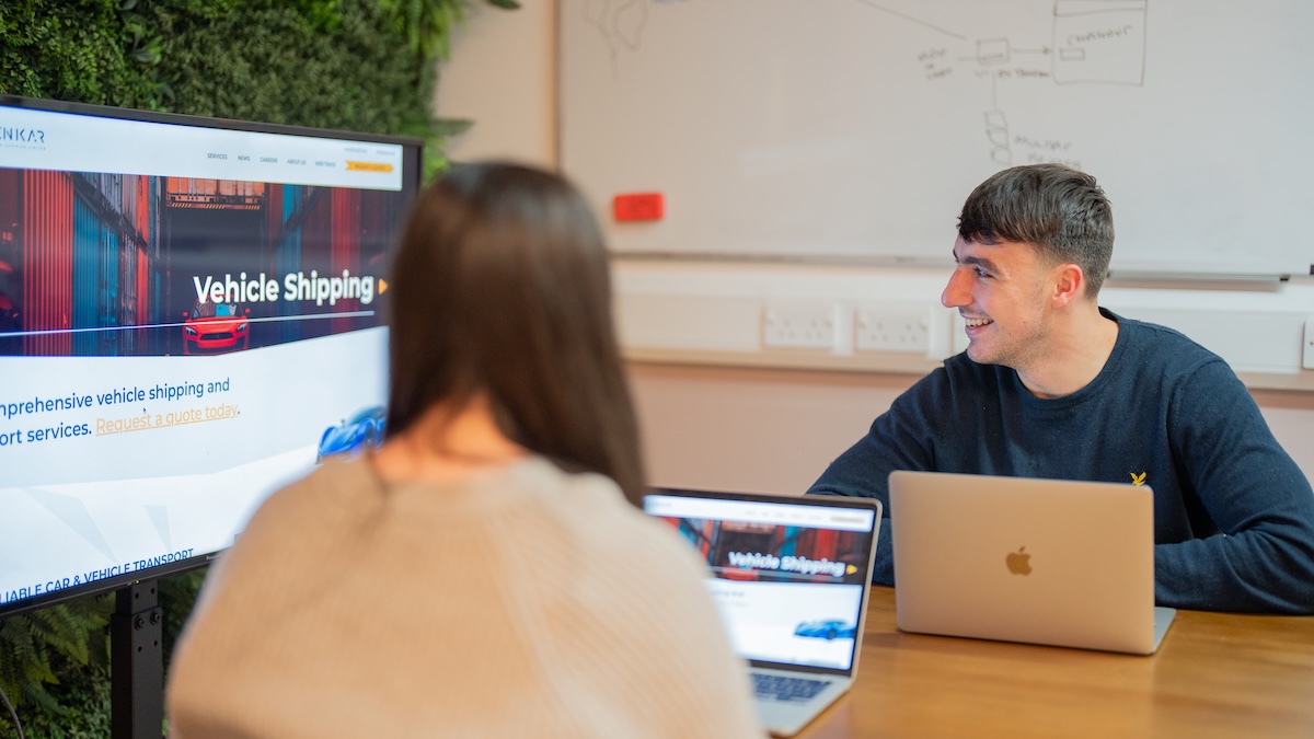 Two people sat with laptops around a TV, featured on a case study on Wonder Agency's WordPress website build for Jenkar Shipping.