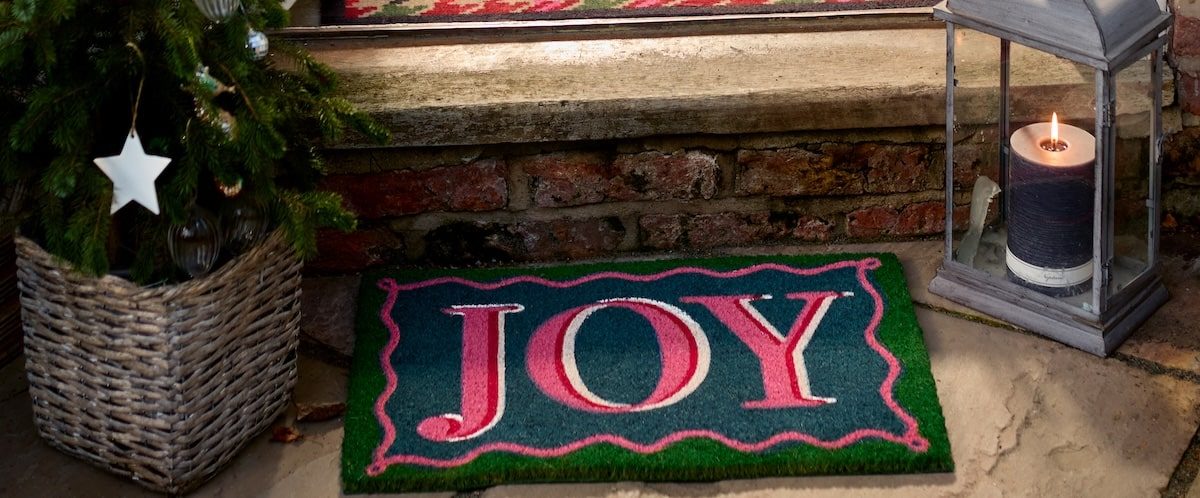 An outdoor doormat that says Joy, featured on a case study on Wonder Agency's custom advent calendar build for Hug Rug